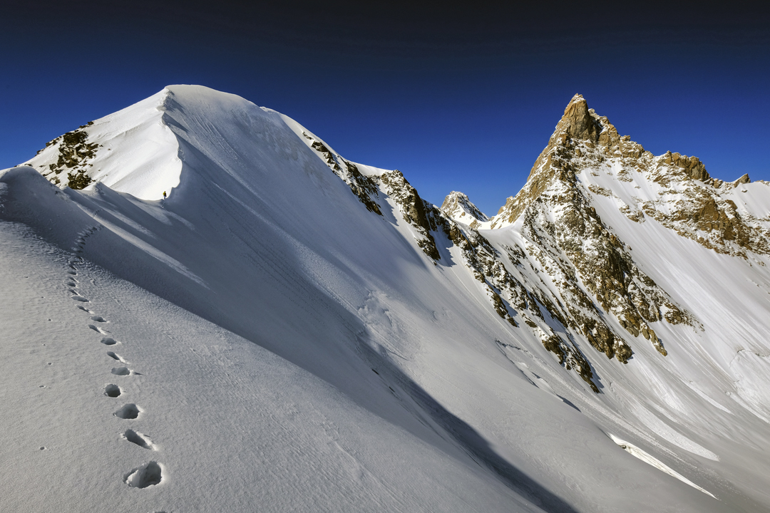 Approaching the dome-like summit (ca. 5700m) south of Peak 6038. From this top, the Slovenian team descended to the saddle on the right and down climbed to their tent. Next morning they climbed back to the saddle, traversed to the left skyline ridge, and climbed the sharp summit. [Photo] Marko Prezelj