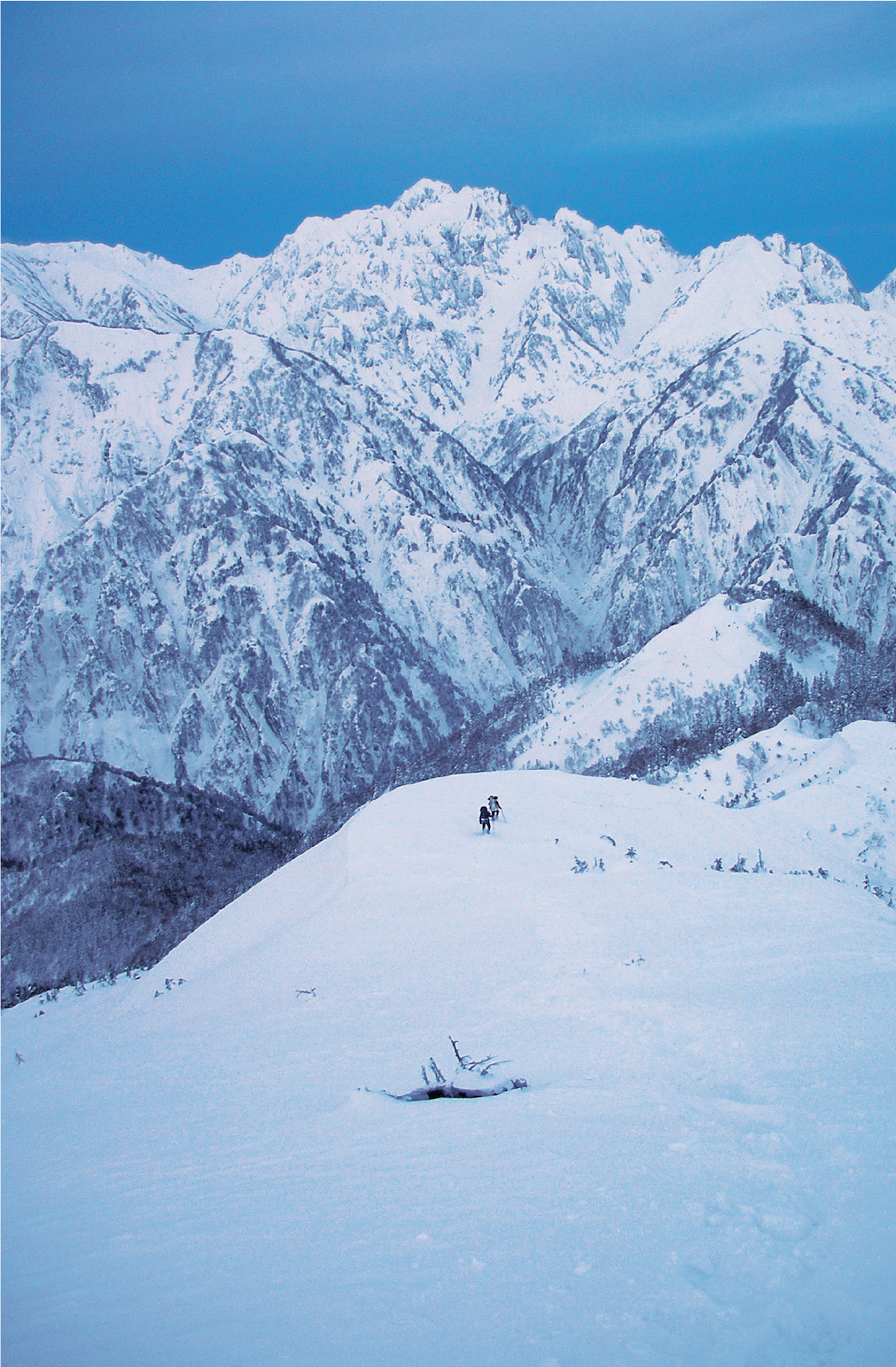 The author and Fumitaka Ichimura play Pachinko on the Kurobe Traverse, Japanese Alps. The apex of the traverse, Mt. Tsurugi (2999m), symbol of Japanese mountaineering, is visible as the highpoint in the distance. From where they are in this photo, the climbers have to descend to the Kurobe River, cross the next mountain and then keep climbing to Mt. Tsurugi. They managed the traverse in the heart of winter in fourteen days. [Photo] Yusuke Sato