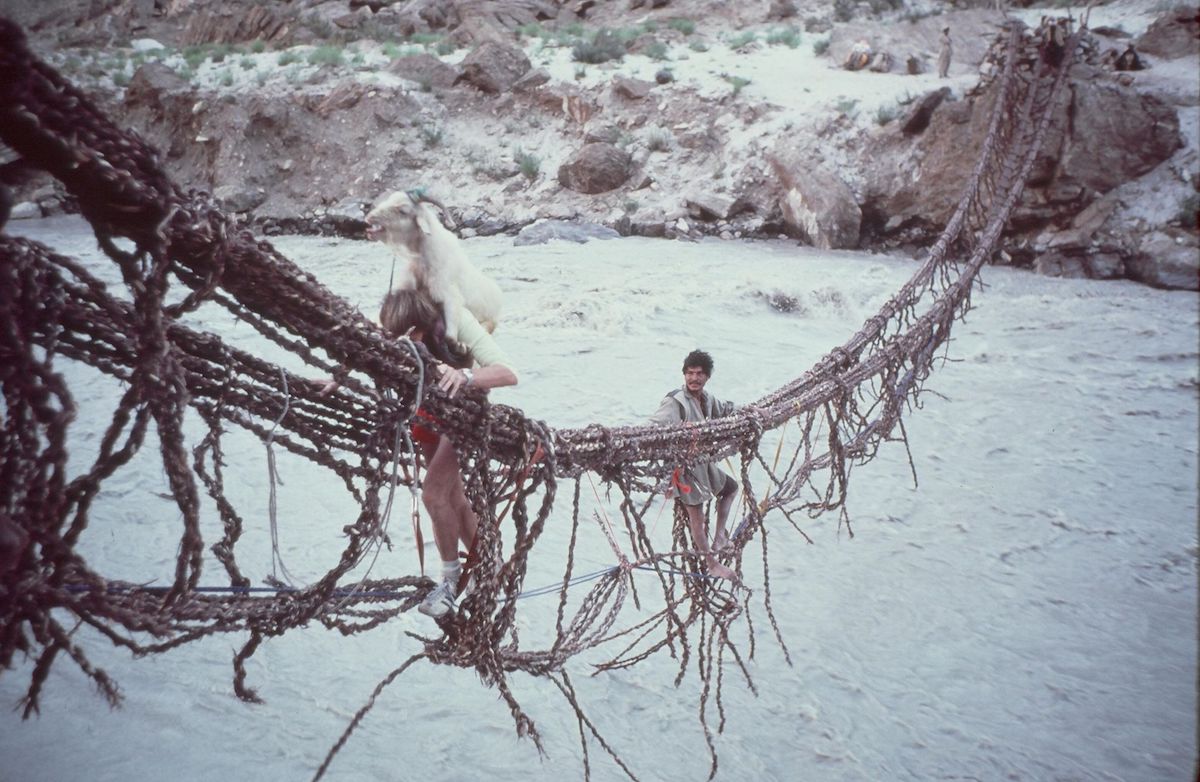 John Roskelley carrying a live goat on his back across the Dumordu River during the approach to Great Trango Tower, Pakistan, 1977. [Photo] Galen Rowell, Kim Schmitz collection