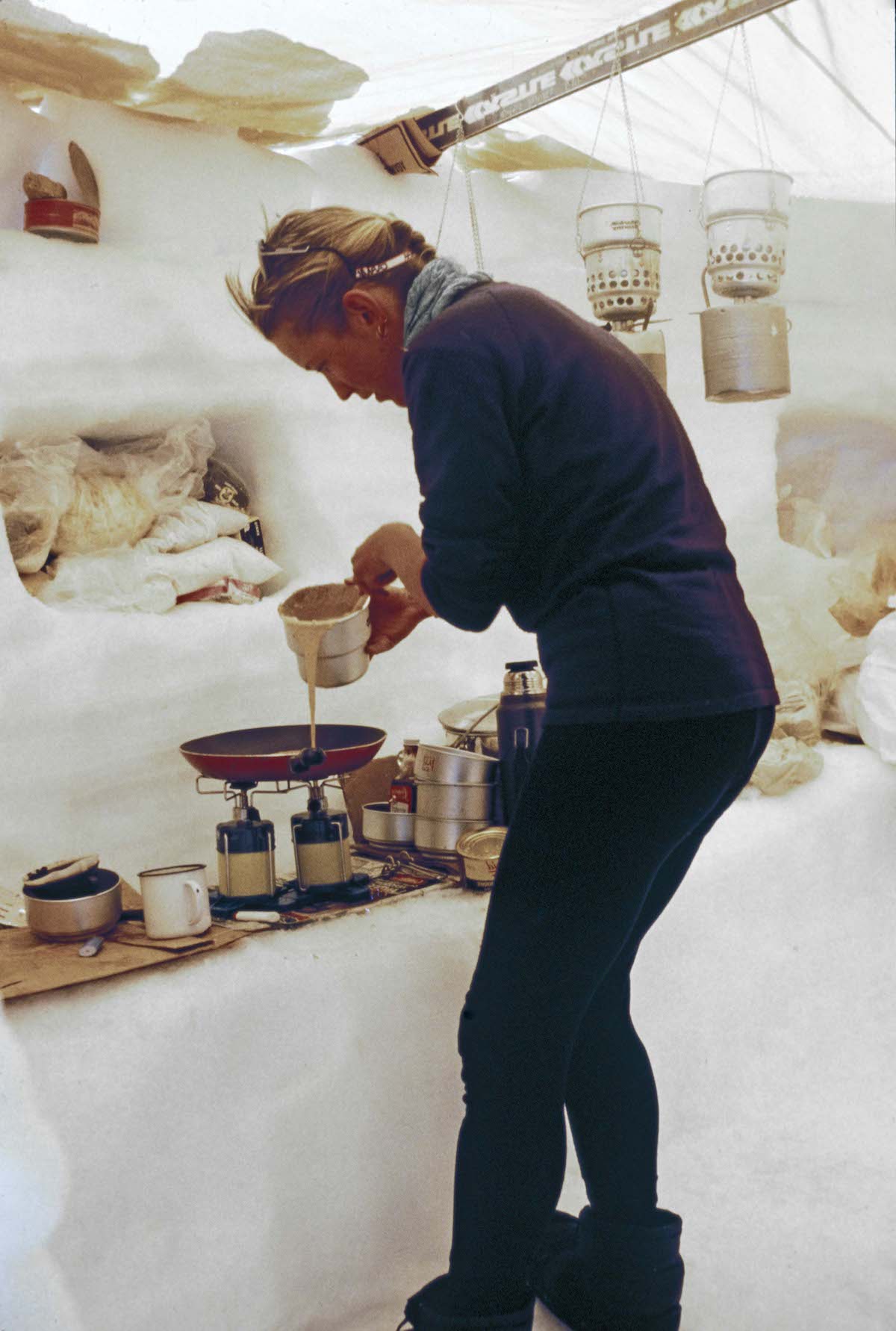Photo caption reads, “Jane makes pancakes in our kitchen shelter at Camp Two.” [Photo] Jim Elzinga, courtesy of Mountaineers Books