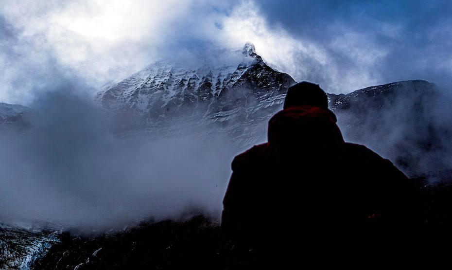 Ethan Berman looking at the Emperor Face from their camp by the river. This was the best view he and Uisdean Hawthorn had before the mist returned. The Texqakallt Nation name for the 3954-meter peak, Yexyexescen, roughly translates to striped rock, a reflection of the multilayered horizontal striations. [Photo] Uisdean Hawthorn