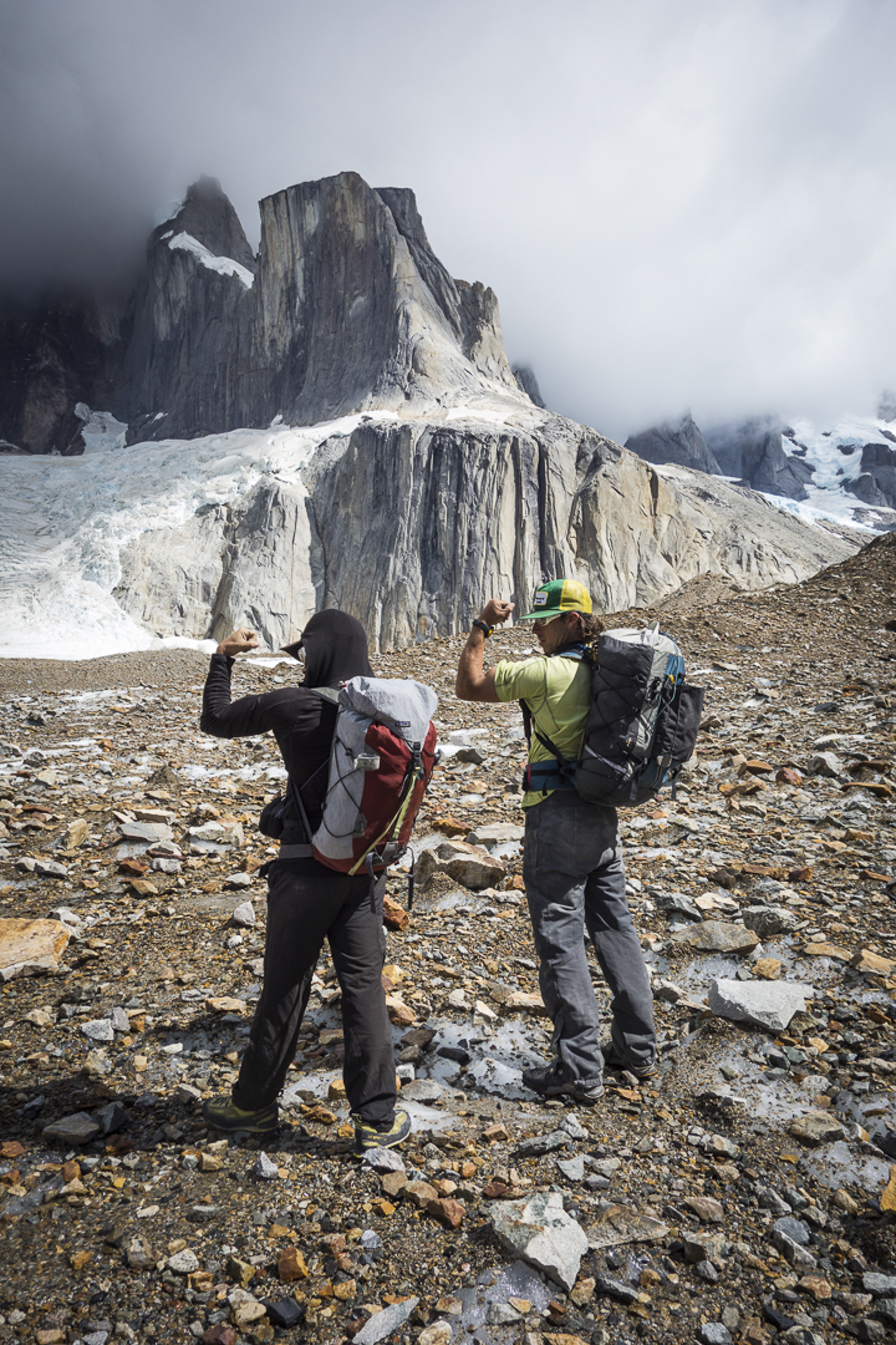 Mikey Schaefer and Josh Huckaby flex after climbing El Mocho (1953m), pictured in the background. Huckaby writes, Together with Kate Rutherford in 2013 we climbed Voie Des Benitiers (7b+ or 6c [5.12c or 5.11b] C1, 400m) along the sun-shade line in the photo. [Photo] Kate Rutherford