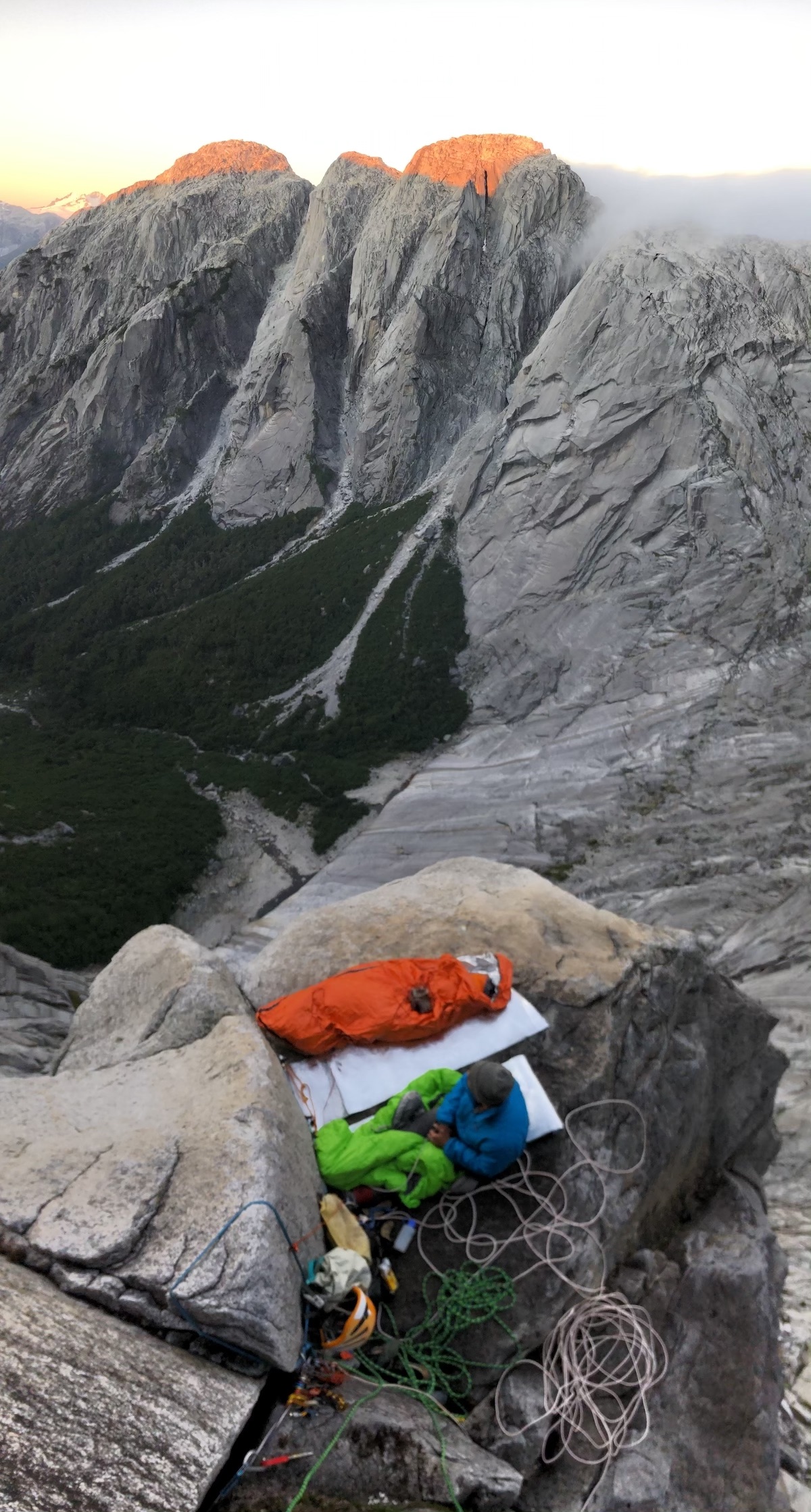 Powell settles into our airy bivy, one pitch up the headwall of Cerro Walwalun. The last light of day is shining on Cerro Milton Adams (left) and Cerro Laguna (right). In the top right, clouds pour in from the Monster Valley over the pass that separates Anfiteatro and Trinidad valleys. Right of center, you can see the broken terrain and low-angle slabs that Chip and I ascended to arrive at our perch. [Photo] Chris Kalman