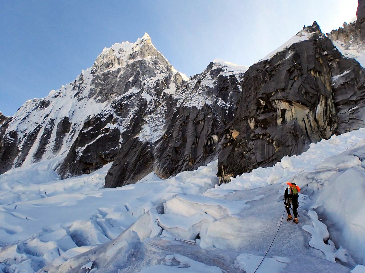 Steve Skelton underneath the imposing southwest face of Tualliraju headed to the base of the Guides Route. [Photo] Ben Dare