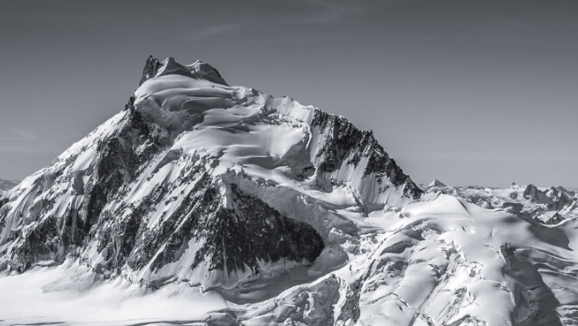The Epaulette (West) Ridge of Mt. Waddington follows the right skyline. The bergschrund that the climbers jumped down at the end of the ridge below the summit is visible as a shadowed line, just below the horizon on the white slope. [Photo] Courtesy of John Scurlock